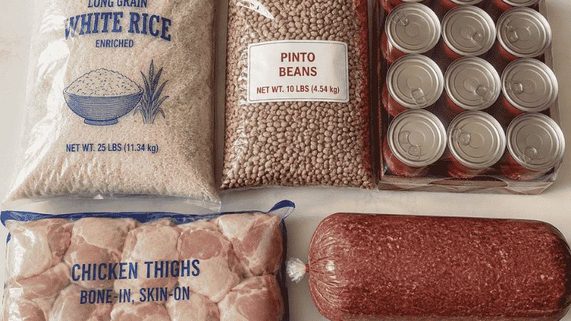 Bulk grocery ingredients for big family meals cheap: 25-lb rice bag, 10-lb dried beans, multi-pack canned tomatoes, and large packs of chicken thighs and ground beef