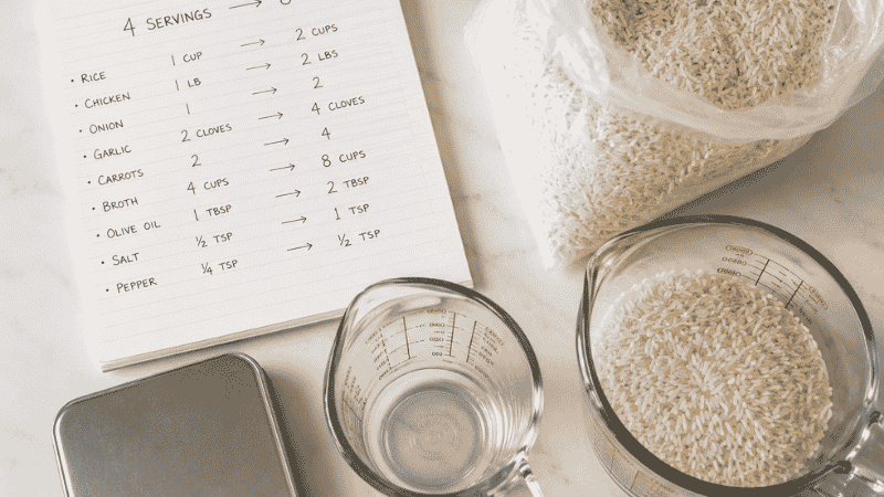 Recipe scaling notepad with conversion chart from 4 to 8 servings beside a measuring cup and kitchen scale — a practical guide for scaling up big family meals cheap