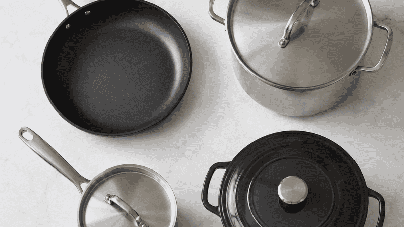 Four essential cookware pieces for a family kitchen: 12-inch non-stick skillet, stock pot, saucepan, and enameled Dutch oven arranged on a white surface