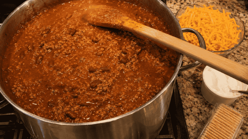 A large stock pot of beef and bean chili on the stovetop with toppings ready beside it — a cheap one-pot meal for large families that feeds 10 to 12 people for under $14