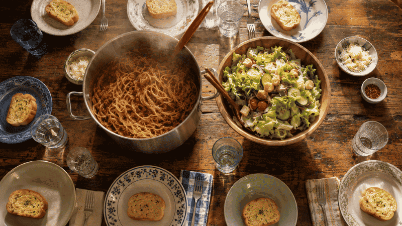 Large family dinner table set for 8 with a pot of spaghetti and meat sauce in the center — a cheap meal for large families that feeds 8 people for under $11 total