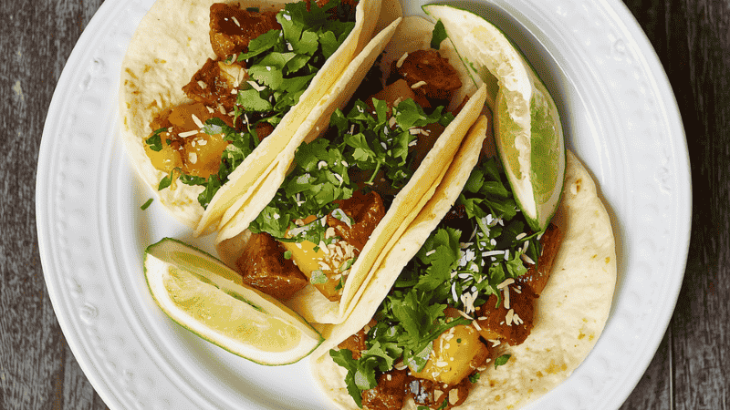A finished plate of authentic chorizo and potato tacos topped with fresh cilantro and lime wedges, served on a rustic wooden table.