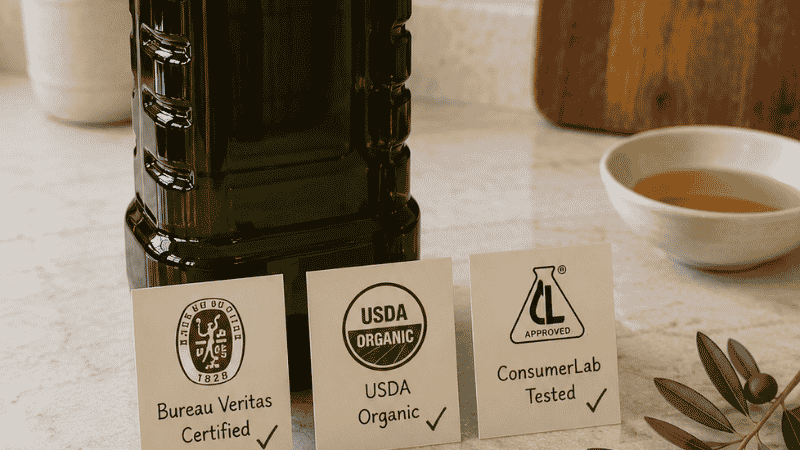 Large Kirkland Organic EVOO 2-liter jug with three certification cards showing Bureau Veritas certified, USDA Organic, and ConsumerLab tested — the best overall Kirkland olive oil at $0.34 per oz