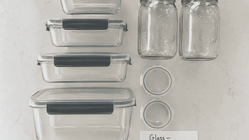 Meal prep container setup showing glass rectangular containers with snap lids, wide-mouth mason jars for soups, and small condiment cups for dressings — the recommended container system for weekly lunch prep