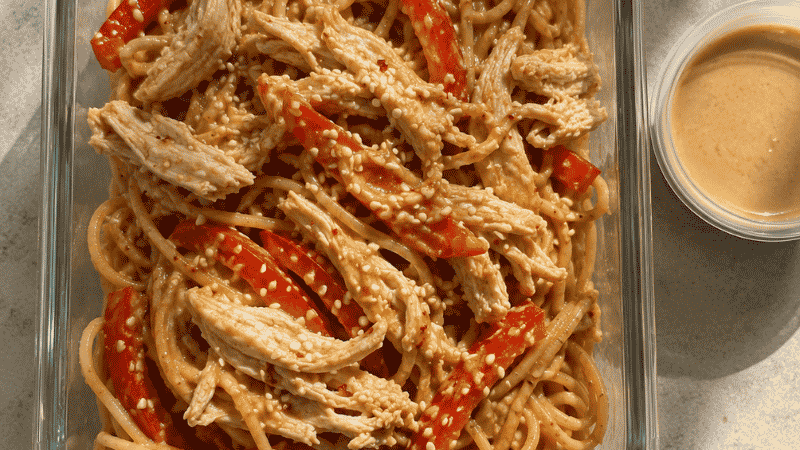 Glass meal prep container with cold sesame noodle bowl — spaghetti in peanut sesame sauce topped with shredded chicken and sliced bell pepper — a budget meal prep lunch under $2.30 per serving